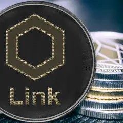 Nahaufnahme einer Chainlink Coin mit dem Schriftzug "Link" und einem sechseckigen Symbol. Daneben stapeln sich weitere Kryptomünzen.