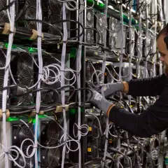Ein Mann mit Kopfhörern arbeitet an einer Wand voller Lüfter und Kabel. Dies zeigt, wie funktioniert krypto mining: leistungsstarke Computer lösen komplexe Rätsel.