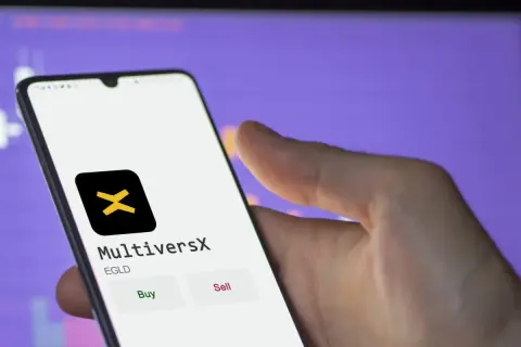 Hand hält Smartphone mit MultiversX App, die EGLD-Token anzeigt. Kauf- und Verkaufsoptionen sind sichtbar.