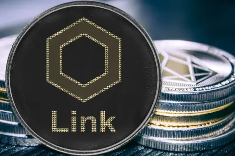Nahaufnahme einer Chainlink Coin mit dem Schriftzug "Link" und einem sechseckigen Symbol. Daneben stapeln sich weitere Kryptomünzen.