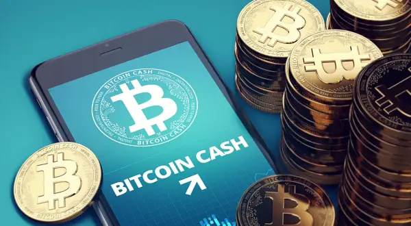 Smartphone zeigt Bitcoin Cash, daneben stapeln sich goldene Bitcoin Cash Münzen.