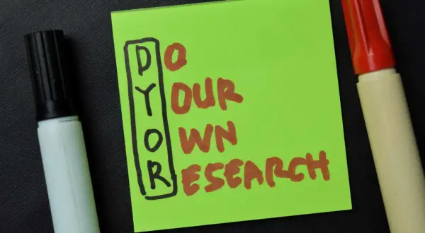 Grüne Notiz mit der Aufschrift "DYOR" (Do Your Own Research) und zwei Markern. Die DYOR Bedeutung ist klar: Eigeninitiative bei der Recherche.