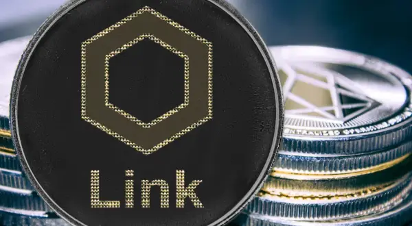 Nahaufnahme einer Chainlink Coin mit dem Schriftzug "Link" und einem sechseckigen Symbol. Daneben stapeln sich weitere Kryptomünzen.