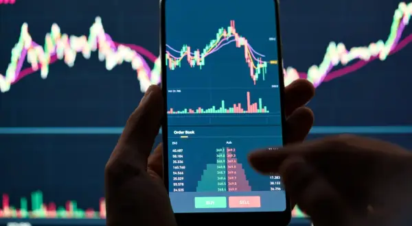 Hand hält Smartphone mit Bitcoin-Chart und Orderbuch. Der Kurs fällt, was auf einen möglichen Bitcoin short hindeutet.