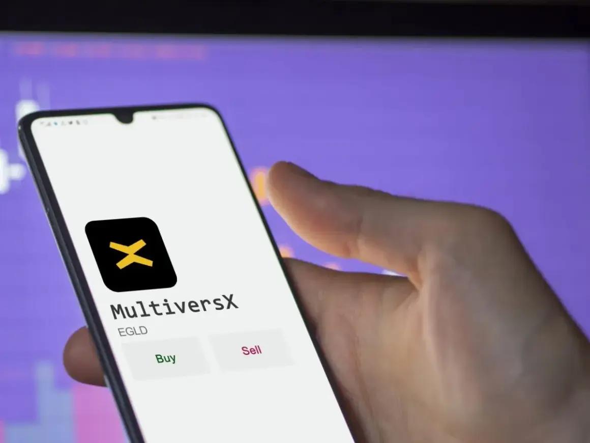 Hand hält Smartphone mit MultiversX App, die EGLD-Token anzeigt. Kauf- und Verkaufsoptionen sind sichtbar.