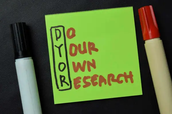 Grüne Notiz mit der Aufschrift "DYOR" (Do Your Own Research) und zwei Markern. Die DYOR Bedeutung ist klar: Eigeninitiative bei der Recherche.